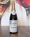 Bottle of wine labelled 'Kingfisher Kiss Sparkling White 2023 Wine of England' on a wooden surface with a colourful abstract wine glass background