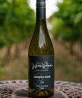 A bottle of Wressle Vineyard Hammered Heron 2025 white wine stands on a decorative metal table in a vineyard with blurred green grapevines in the background.
