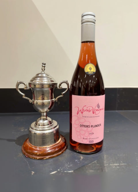 Bottle of Wressle Vineyard Otters Plunder 2024 rose wine next to a silver trophy on a marble worktop.