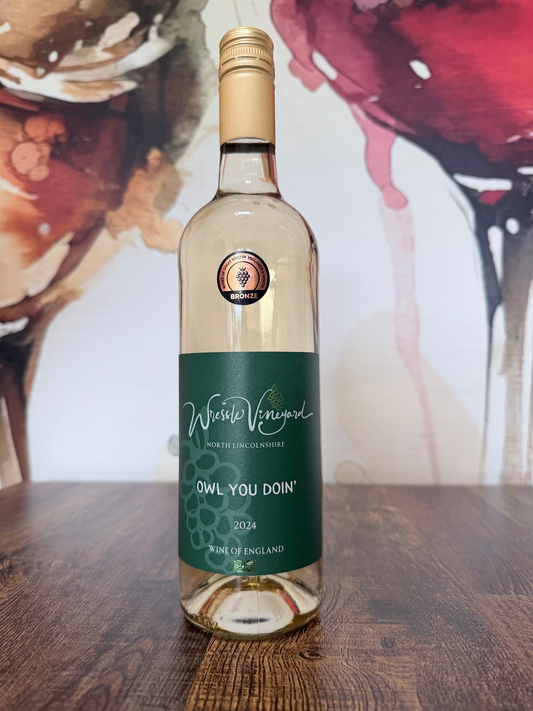 Wine bottle labelled 'Owl You Doin 2024' on a wooden surface with an abstract wine glass background