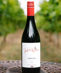 A bottle of Wressle Vineyard Foxed Red 2025 wine stands on a decorative metal table with a blurred outdoor vineyard background.
