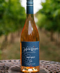 A bottle of Wressle Vineyard Holy Moley 2023 rosé wine stands on a metal patio table with a blurred vineyard background.