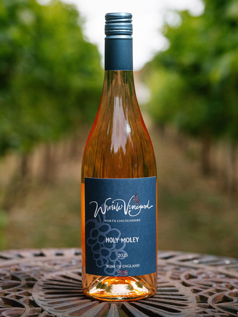 A bottle of Wressle Vineyard Holy Moley 2023 rosé wine stands on a metal patio table with a blurred vineyard background.