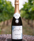 A bottle of Wressle Vineyard Kingfisher Kiss 2023 Sparkling White wine stands on a metal patio table with a blurred vineyard background.