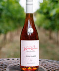 A bottle of Wressle Vineyard Otters Plunder 2023 wine standing on a metal table with a blurred vineyard background.