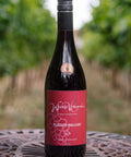 A bottle of Wressle Vineyard 'Plucked Pheasant' 2024 red wine, set on a decorative metal table with a blurred vineyard background.