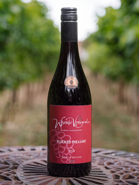 A bottle of Wressle Vineyard 'Plucked Pheasant' 2024 red wine, set on a decorative metal table with a blurred vineyard background.