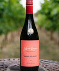 A bottle of Wressle Vineyard Robbing Red Breast 2023 red wine stands on a metal patio table with a blurred vineyard background.