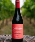 A bottle of Wressle Vineyard Robbing Red Breast 2025 red wine stands on a metal patio table with a blurred vineyard background.